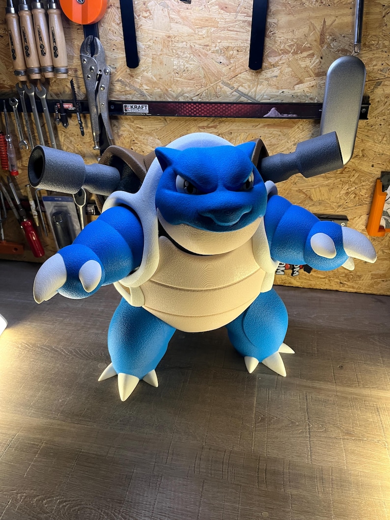 May include: A large, blue and white Blastoise figure, a popular character from the Pok&eacute;mon franchise. The figure has a detailed design, with its signature cannons on its back and white spikes on its limbs. The figure is standing on a wooden surface.