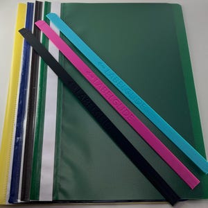 Könnte beinhalten: Eine Sammlung mehrfarbiger Dokumentenmappen aus Kunststoff mit passenden dünnen, länglichen Kunststoffstreifen, die mit LABELGUIDE beschriftet sind. Die Mappen sind in Gelb, Blau, Schwarz, Weiß und Grün gestapelt, mit diagonalen Streifen.