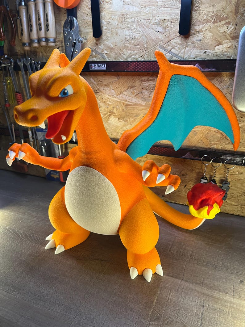 May include: A vibrant orange Charizard figurine with blue wings and white claws. The figurine has a cream-colored belly and is holding a red and yellow flame. The figure is a popular character from the Pokemon franchise.