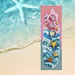Puede incluir: Un marcapáginas hecho a mano con temática de playa. El marcapáginas tiene un fondo rosa y azul con conchas bordadas, una estrella de mar y olas. El diseño es rectangular y parece estar bordado a punto de cruz.