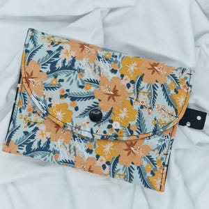 May include: A small floral patterned fabric pouch with a black button closure. The pouch is made of a soft, cotton fabric and has a blue, green, and orange floral print.