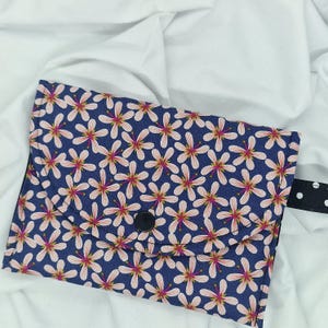 Può includere: Una pochette in tessuto blu con un motivo floreale bianco e una chiusura a bottone nero. La pochette ha una patta che si ripiega e si fissa con il bottone. La pochette è realizzata in un tessuto morbido e resistente, ideale per riporre piccoli oggetti.