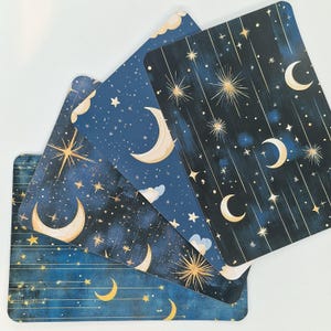 Op de afbeelding: Vier rechthoekige kaarten met afgeronde hoeken, met een hemels ontwerp. De kaarten tonen een marineblauwe achtergrond versierd met gouden sterren, maan en wolken. Het algemene thema is nachthemel en astrologie.