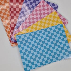 Op de afbeelding: Een verzameling rechthoekige kaarten in verschillende kleuren, elk met een geruit patroon. De kleuren zijn onder meer oranje, rood, paars, roze, geel en blauw. De kaarten zijn in een waaier gerangschikt.