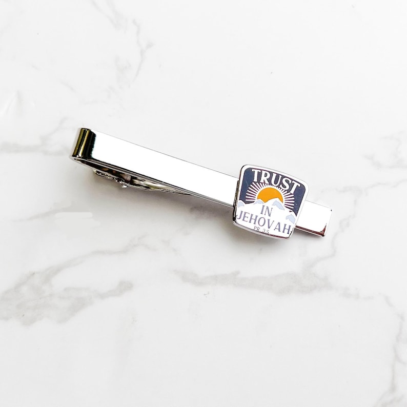May include: Silver tie clip with a blue and white enamel design featuring a sunrise and the text "TRUST IN JEHOVAH PS. 37:3".