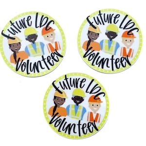 Puede incluir: Tres pegatinas redondas con fondo amarillo y lunares blancos. Cada pegatina presenta una imagen de dibujos animados de tres personas con cascos y el texto "Future LBC Volunteer".