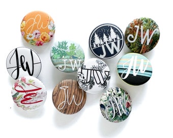 May include: Assortment of 10 round buttons with various designs. The buttons feature floral patterns, a wood grain design, a forest scene, and a striped pattern. Each button has the initials "JW" printed on it.