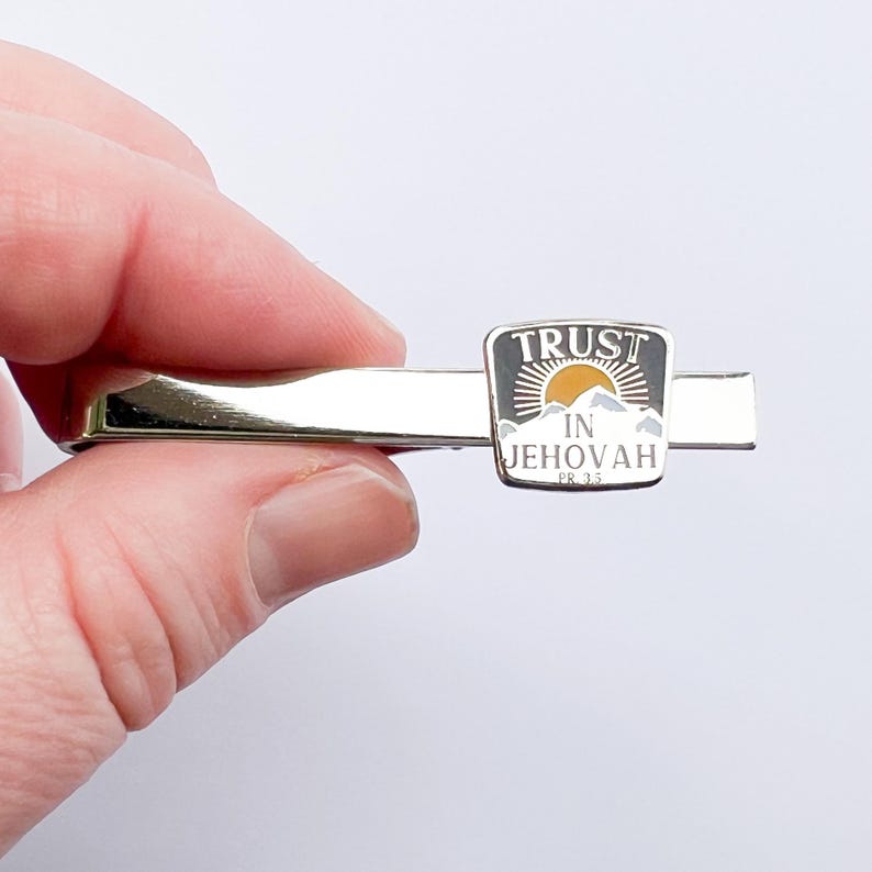May include: Silver tie bar with a black and white enamel design. The design features a mountain range with a sun rising behind it. The text "TRUST IN JEHOVAH PS 33" is printed on the design.
