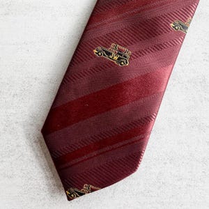 May include: A burgundy striped tie with a gold and black car design. The car has the letters "JW" on the side.