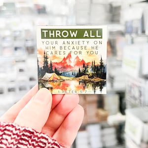 May include: A motivational quote card with a watercolor illustration of a mountain scene with a lake and a tent. The quote reads "Throw all your anxiety on him because he cares for you." The card also includes the scripture reference "1 Peter 5:7".