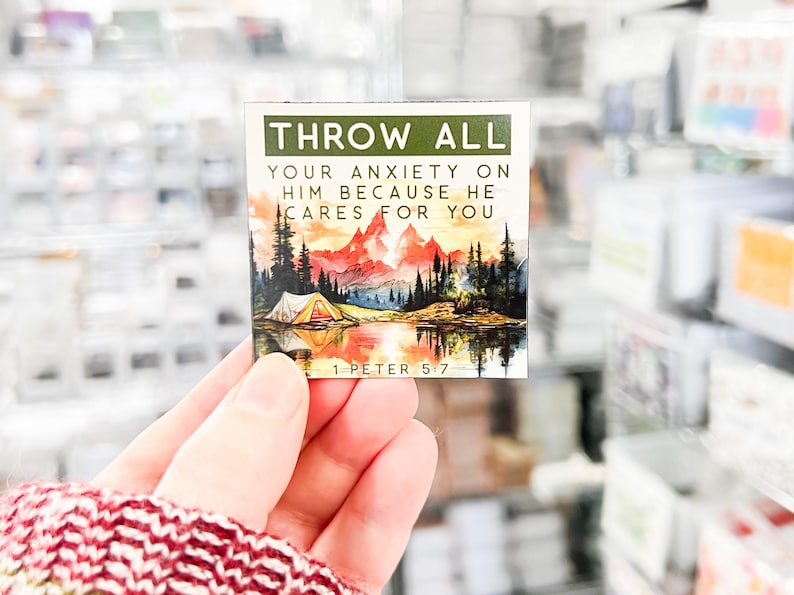 May include: A motivational quote card with a watercolor illustration of a mountain scene with a lake and a tent. The quote reads "Throw all your anxiety on him because he cares for you." The card also includes the scripture reference "1 Peter 5:7".