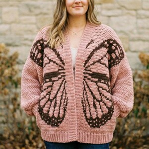 Peut inclure: Cardigan en crochet rose clair, ouvert sur le devant, avec un motif d'ailes de papillon marron foncé. Les ailes de papillon sont bien mises en valeur sur le devant et les manches du pull. C'est un vêtement fait main et confortable.
