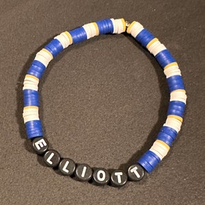 May include: A blue and white beaded bracelet with a gold accent and the name "ELLIOT" spelled out in black beads.