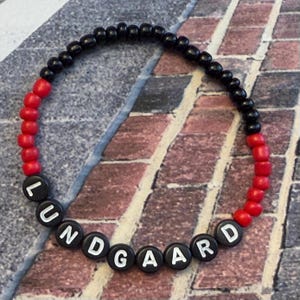 May include: A black and red beaded bracelet with the word "LUNDGAARD" spelled out in white letters on black beads.