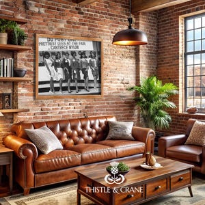 May include: A framed black and white photograph featuring six women standing in a row with the text DU PONT DAY PRETTIEST LEGS AT THE FAIR CANTRECE NYLON displayed above them. The print is mounted on a brick wall above a brown leather sofa.