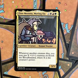 Peut inclure: Une carte Magic: The Gathering personnalis&eacute;e avec Finn Mertens de Adventure Time. La carte a une bordure dor&eacute;e et comprend le texte "Finn Mertens, Moving On" et "Kresh the Bloodbraided". La carte est une cr&eacute;ature l&eacute;gendaire - Human Warrior.