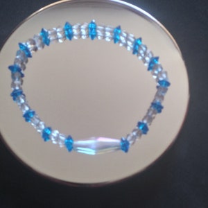 Op de afbeelding: Een blauwe en heldere kralen armband met een iriserende bedel. De armband is gemaakt met kleine, gefacetteerde kralen.