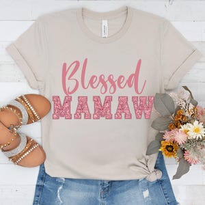 May include: A light beige t-shirt with a pink glitter design that says "Blessed Mamaw".