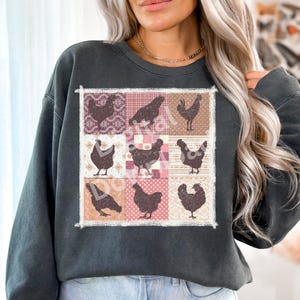 Pode incluir: Uma camisa de frio cinza escura com um design de patchwork que apresenta silhuetas de galinhas em v&aacute;rias poses. O patchwork &eacute; composto por quadrados rosa, branco e marrom com uma variedade de padr&otilde;es.