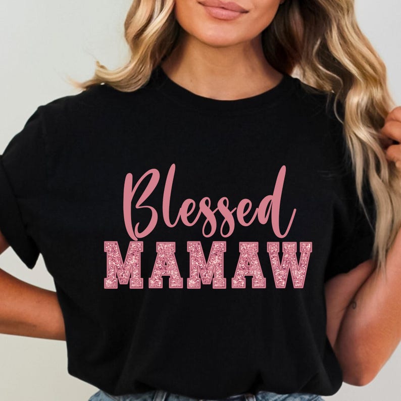 May include: Black t-shirt with the text "Blessed Mamaw" in pink glitter lettering.