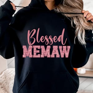 K&ouml;nnte beinhalten: Schwarzer Hoodie mit einem pinkfarbenen Glitzerdesign, auf dem "Blessed Memaw" steht.