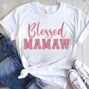 May include: White t-shirt with the text "Blessed Mamaw" in pink glitter lettering.