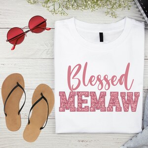 K&ouml;nnte beinhalten: Wei&szlig;es T-Shirt mit dem Text "Blessed Memaw" in pinkfarbenem Glitzer.