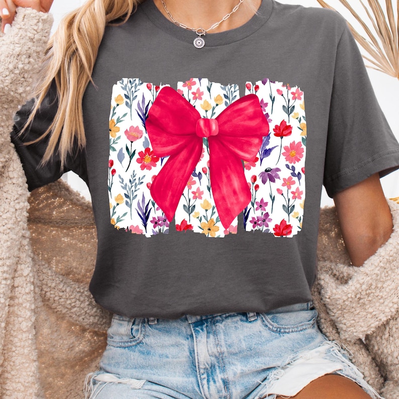 Peut inclure: T-shirt gris fonc&eacute; avec un grand n&oelig;ud rouge sur un motif floral. Le motif floral comprend des fleurs color&eacute;es et des feuilles vertes sur fond blanc. Le t-shirt est de style d&eacute;contract&eacute;.
