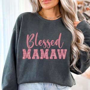 May include: A dark gray sweatshirt with the text "Blessed Mamaw" in pink glitter lettering.