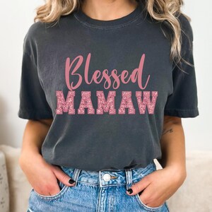 May include: A dark gray t-shirt with the text "Blessed Mamaw" in pink glitter lettering.