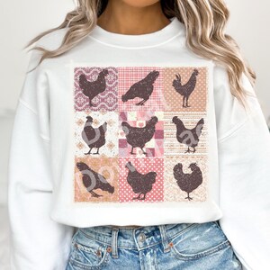 Pode incluir: Uma camisa de moletom branca com um design de patchwork que apresenta silhuetas marrons de galinhas em um fundo rosa e branco.