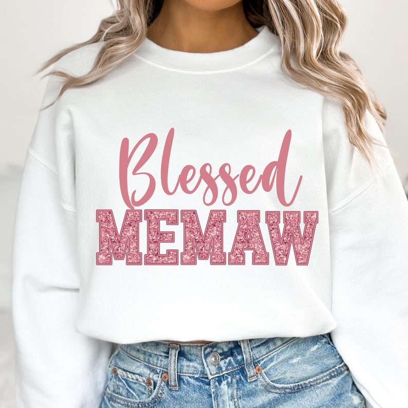 K&ouml;nnte beinhalten: Wei&szlig;er Pullover mit dem Text "Blessed Memaw" in pinkfarbenem Glitzer.