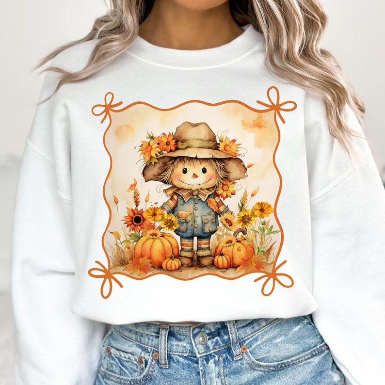 May include: White sweatshirt featuring a watercolor illustration of a scarecrow wearing a hat adorned with sunflowers. The scarecrow is surrounded by pumpkins and more sunflowers, with an orange border.