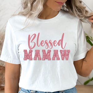 May include: White t-shirt with the text "Blessed Mamaw" in pink glitter lettering.