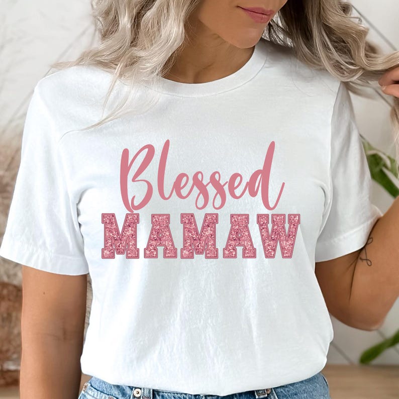 May include: White t-shirt with the text "Blessed Mamaw" in pink glitter lettering.