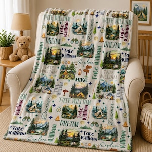 May include: A white fleece blanket featuring a repeating pattern of camping scenes, including tents, pine trees, mountains, and campfires. The design includes the name Tate William, along with the words Dream, Discover, Explore, and Hike.
