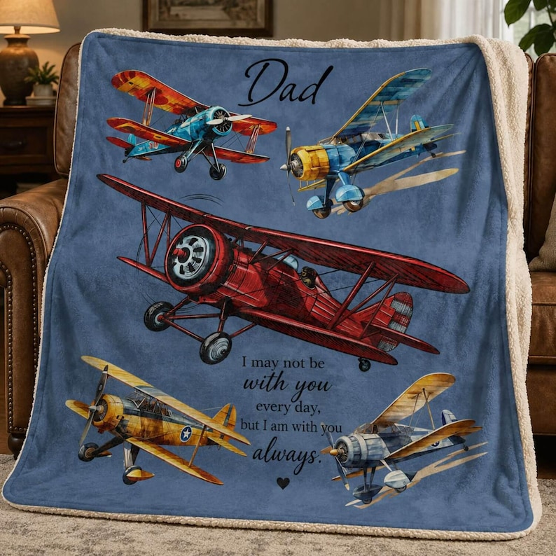 May include: A blue blanket featuring illustrations of vintage airplanes in various colors. The word "Dad" is at the top, with the text "I may not be with you every day, but I am with you always." printed below the airplanes. The blanket has a soft, white sherpa lining.