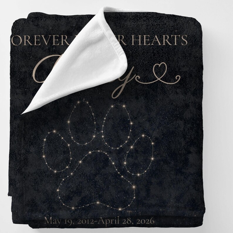 May include: Black blanket with a paw print design made of small, glowing dots. The blanket has the words "Forever in our hearts" and a name in a cursive font. The dates "May 19, 2012-April 28, 2026" are printed at the bottom.