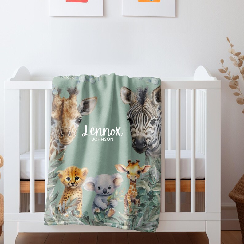May include: A soft sage green baby blanket featuring watercolor illustrations of a giraffe, a zebra, a cheetah cub, a koala, and a small giraffe. The blanket displays the name Lennox and the surname Johnson in white script and block text.