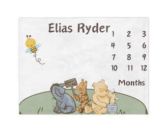 Könnte beinhalten: Eine Winnie Puuh-Baby-Meilenstein-Decke mit grünem Hintergrund und weißem Rand. Die Decke zeigt Winnie Puuh, Tigger und Esel. Die Decke hat auch eine Biene und ein Schild mit der Aufschrift "Bounce This Way". Die Decke hat eine Tabelle, um das Wachstum eines Babys von 1 bis 12 Monaten zu verfolgen.