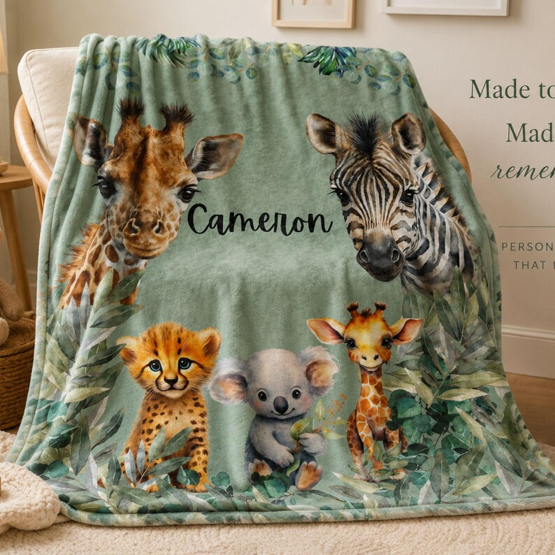 May include: A soft sage green throw blanket featuring a printed illustration of a giraffe, zebra, cheetah cub, koala, and a smaller giraffe surrounded by green foliage. The name Cameron is printed in black script in the center of the blanket.