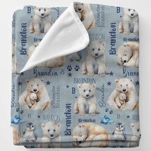 Puede incluir: Una manta para bebé azul y blanca con un patrón repetido de osos polares, pingüinos y estrellas. La manta está personalizada con el nombre "Brandon" en una fuente de letra azul.