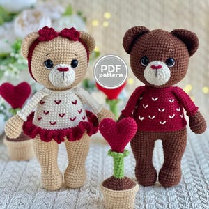 May include: Two crocheted teddy bears, one tan and one brown, stand side-by-side. The tan bear wears a white dress with red heart accents and a red headband. The brown bear wears a red sweater with white heart accents. Each bear holds a crocheted heart.