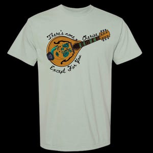May include: A light green t-shirt featuring a detailed illustration of a mandolin with a floral design. The mandolin is brown and gold, with green and blue accents. The text "There's none Cherise Except For You" is written around the mandolin.