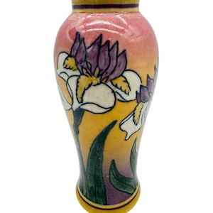 May include: A small ceramic vase with a floral design. The vase has a pink and yellow gradient background with a purple and white iris flower design. Green leaves and a yellow rim complete the design.