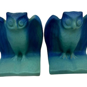 May include: A pair of bookends featuring owls with spread wings, each perched atop an open book. The figures are finished in a gradient color scheme that transitions from a deep royal blue at the top to a lighter turquoise green at the base.