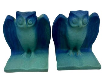 May include: A pair of bookends featuring owls with spread wings, each perched atop an open book. The figures are finished in a gradient color scheme that transitions from a deep royal blue at the top to a lighter turquoise green at the base.