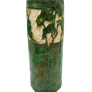 Può includere: Un vaso cilindrico in ceramica con una smaltatura verde testurizzata e maculata. La sezione superiore presenta una fascia incavata color crema non smaltata con un motivo in rilievo verde scuro raffigurante forme vegetali.