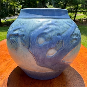 May include: A spherical ceramic vase featuring a matte finish with a gradient of light blue and soft white tones. The surface is decorated with a raised, embossed relief pattern of swirling, organic shapes that wrap around the entire body.