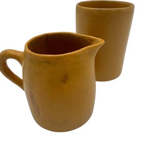 Könnte beinhalten: Ein Set aus zwei Keramik-Küchenutensilien in senfgelber Farbe. Das Set enthält eine Kanne und eine hohe zylindrische Tasse.